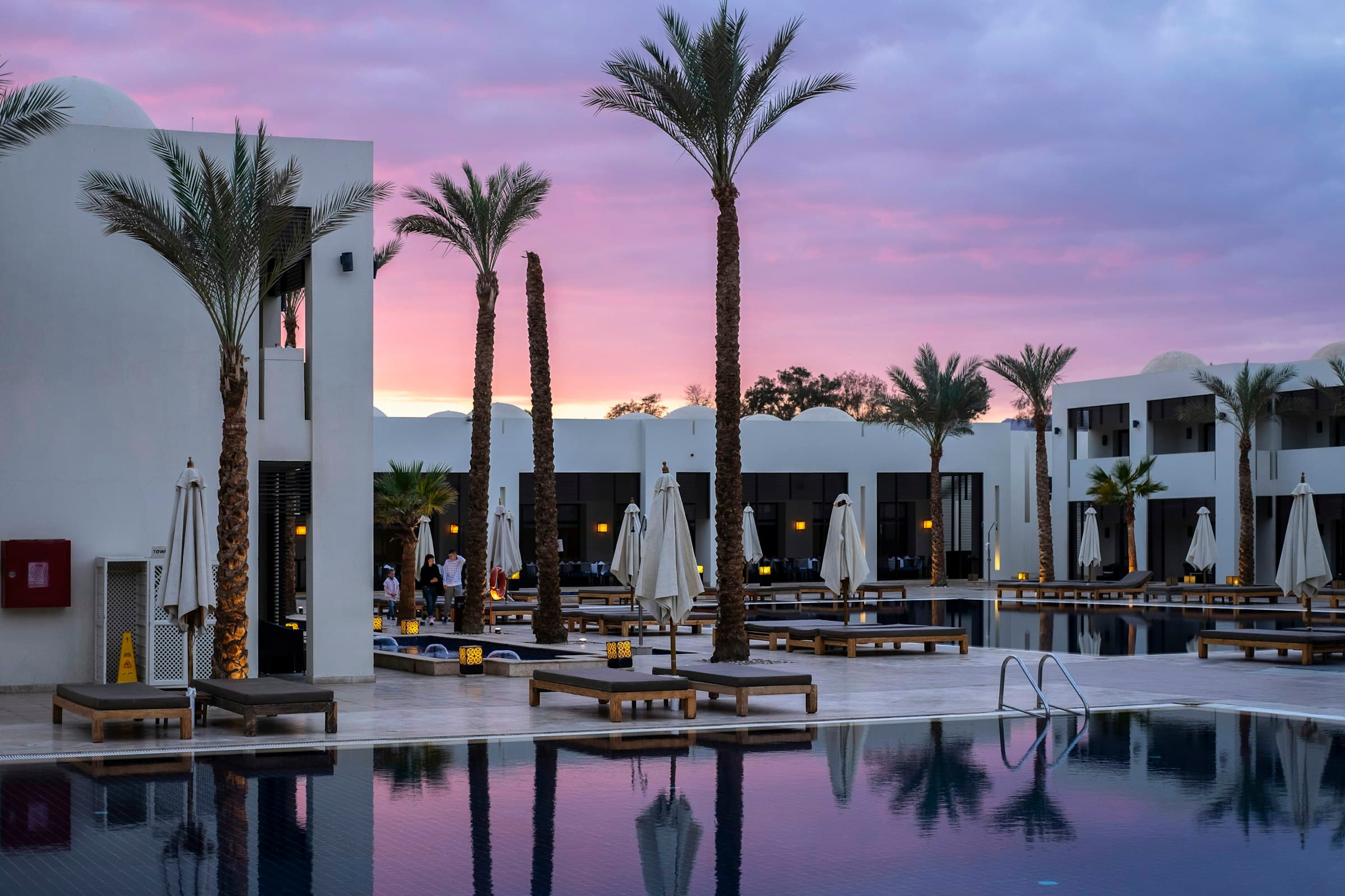 Hotel pool lined with palm trees at dusk